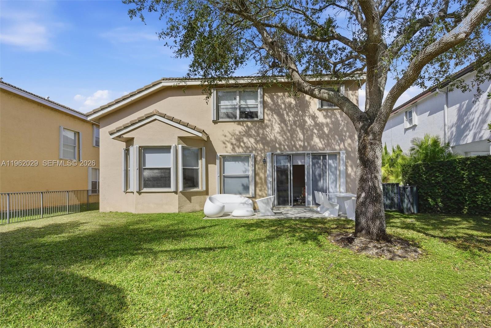The rear exterior of a two-story beige house features a patio, lawn, and large tree — 16460 SW 30th Street, Miramar FL 33027, MIRAMAR, FL