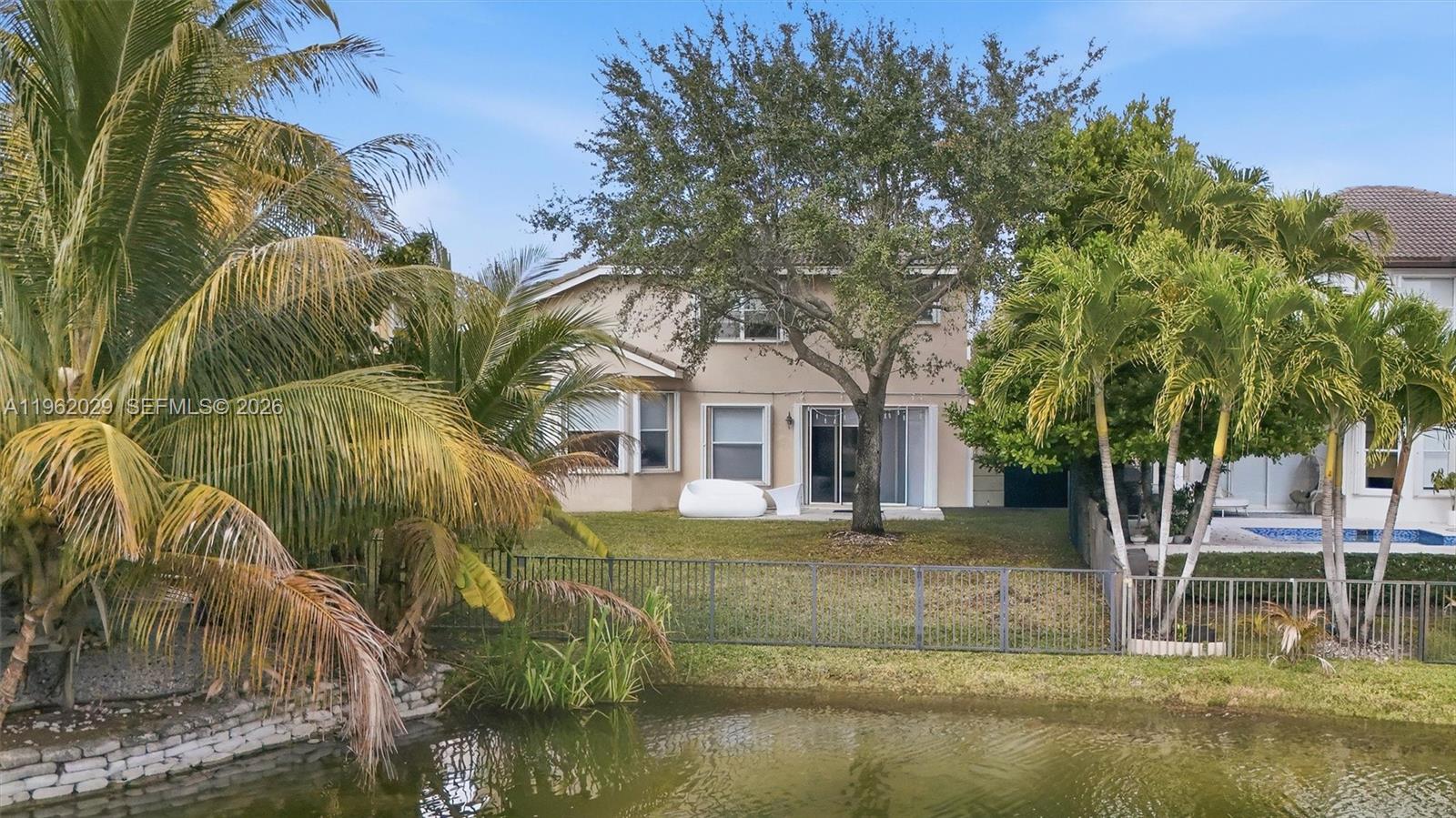 A two-story house with a backyard lawn and palm trees overlooks a small pond — 16460 SW 30th Street, Miramar FL 33027, MIRAMAR, FL