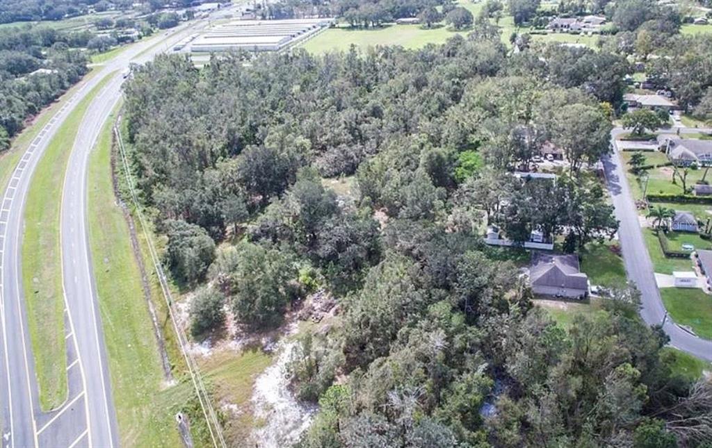 An aerial view shows a wooded lot situated between a highway and a residential street — 9232 US HIGHWAY 98 N, LAKELAND, FL