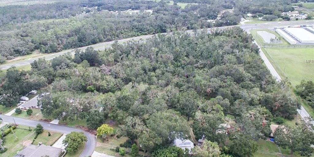 An aerial view shows a densely wooded lot bordered by a road and residential houses — 9232 US HIGHWAY 98 N, LAKELAND, FL