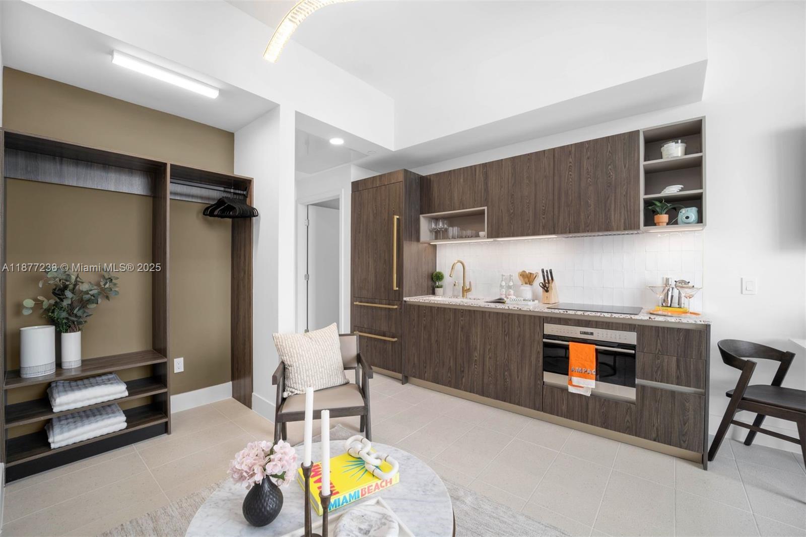 A modern studio apartment features a kitchenette with wood cabinetry and an open closet area — 159 NE 6th St # 5112, Miami FL 33132, MIAMI, FL