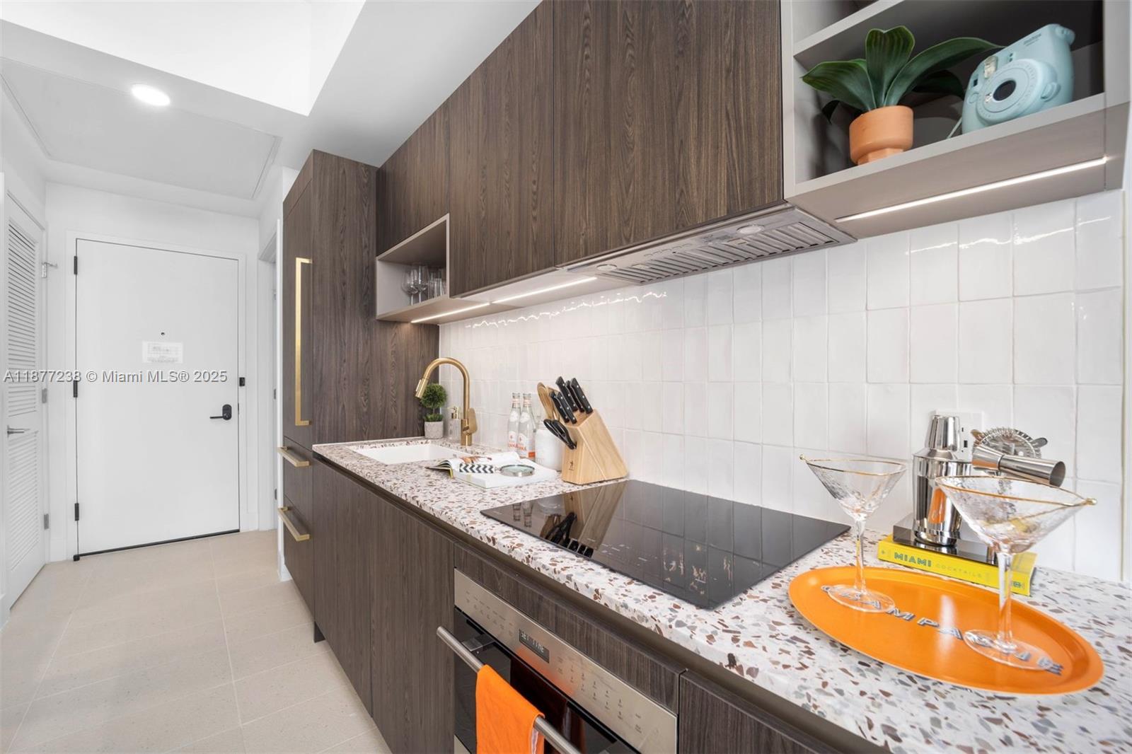 A modern kitchen features dark wood cabinetry, a speckled countertop, and a white tiled backsplash — 159 NE 6th St # 5112, Miami FL 33132, MIAMI, FL
