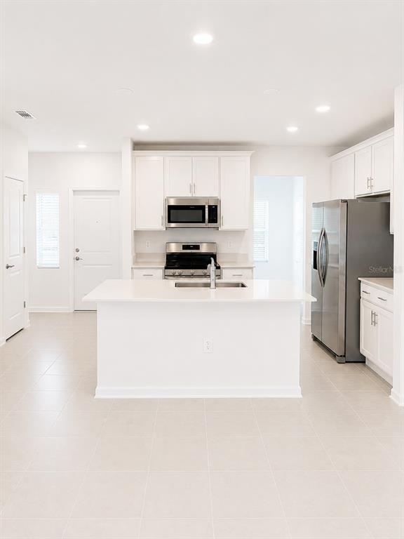 A modern kitchen features white cabinetry, stainless steel appliances, and a central island with seating — 5677 LIVELINESS ALLEY, CLERMONT, FL