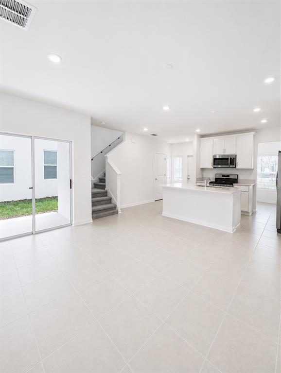 An open-concept kitchen and living area with tile flooring, a staircase, and sliding glass doors — 5677 LIVELINESS ALLEY, CLERMONT, FL