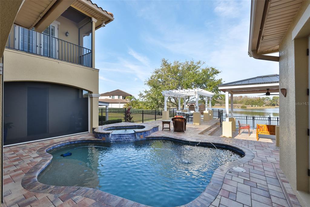 A backyard features a swimming pool, a spa, a pergola, and a view of a lake — 10517 TARPON SPRINGS ROAD, ODESSA, FL