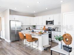 A modern kitchen features white cabinetry, stainless steel appliances, and a central island with barstools — 4519 TRINITY WAY UNIT THC2, KISSIMMEE, FL