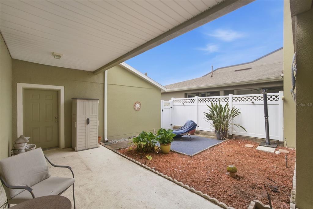 A covered concrete patio overlooks a small fenced backyard with mulch and a lounge chair — 224 WOODHOUSE LANE, DELAND, FL