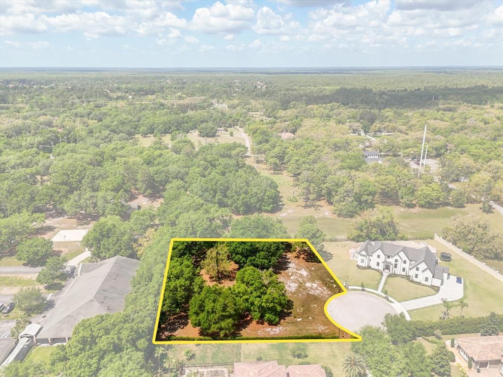 An aerial view shows a wooded, undeveloped lot outlined in yellow next to a house — 1657 ENCLAVE COVE, LAKE MARY, FL