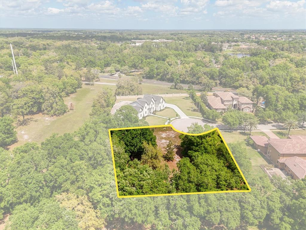 An aerial view shows a wooded, undeveloped residential lot outlined in yellow near suburban homes — 1657 ENCLAVE COVE, LAKE MARY, FL
