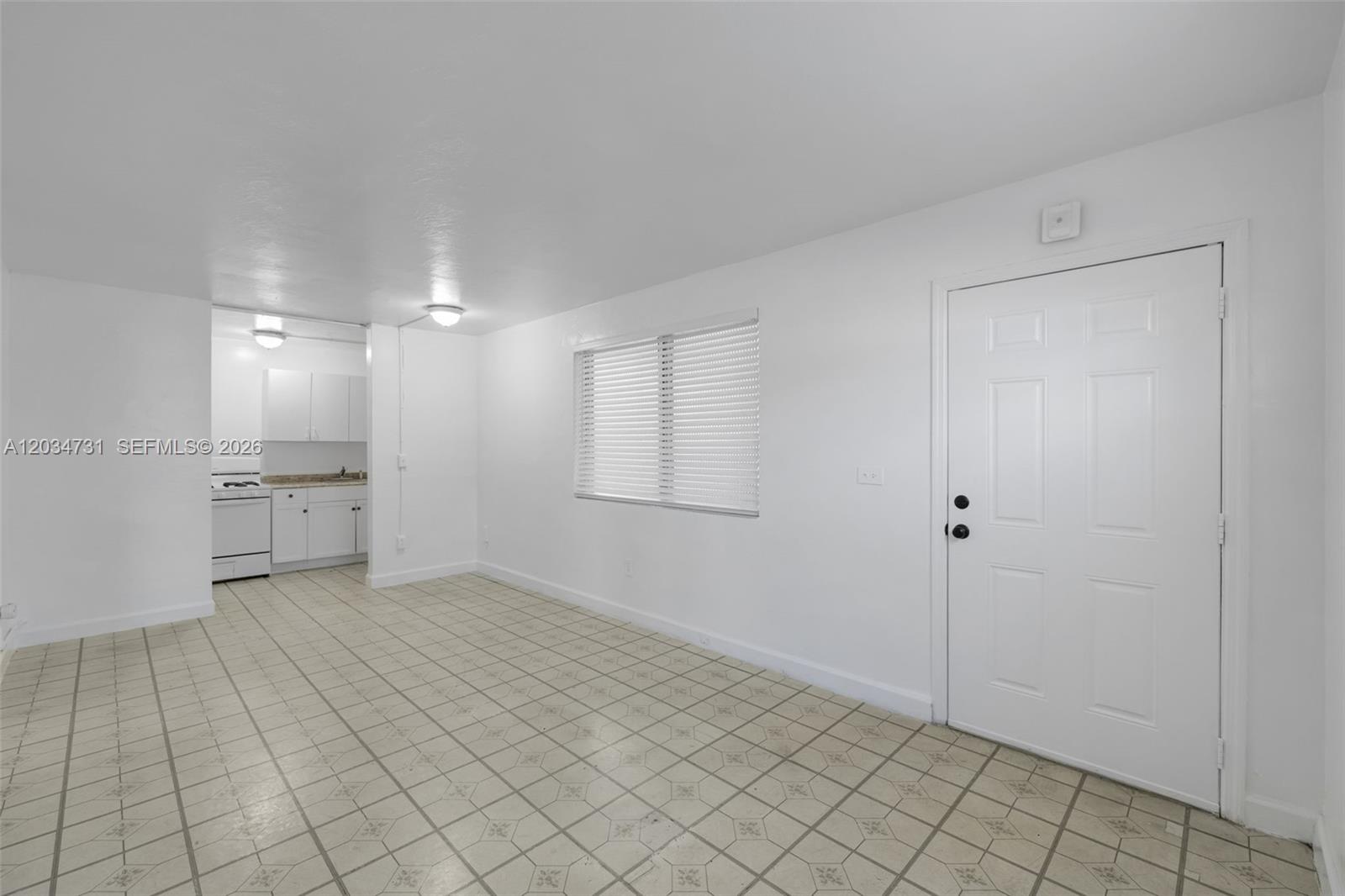 A white-walled room features tiled flooring, a window with blinds, and an adjacent kitchen area — 126 SW 18th Ave # 4, Miami FL 33135, MIAMI, FL