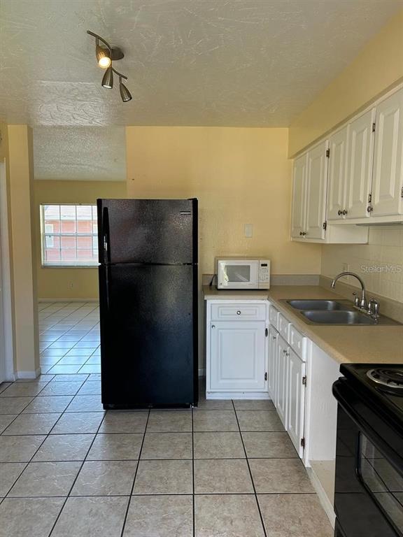 A kitchen features white cabinets, a black refrigerator, a microwave, and light-colored tile flooring — 1627 W OAK RIDGE ROAD UNIT D, ORLANDO, FL