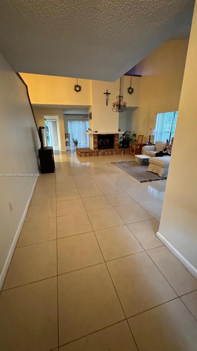 A tiled living room features a brick fireplace, a vaulted ceiling, and a chandelier — 15039 SW 89th Terr Rd, Miami FL 33196, MIAMI, FL