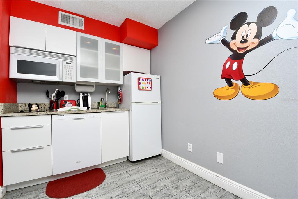 A small kitchen features white cabinets, a microwave, a dishwasher, and a Mickey Mouse wall decal — 3100 PARKWAY BOULEVARD UNIT 315, KISSIMMEE, FL