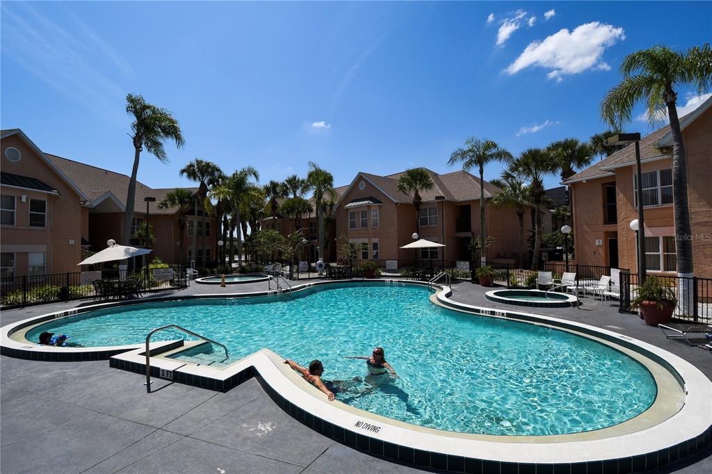 An outdoor swimming pool with a hot tub is surrounded by apartment buildings and palms — 3100 PARKWAY BOULEVARD UNIT 315, KISSIMMEE, FL