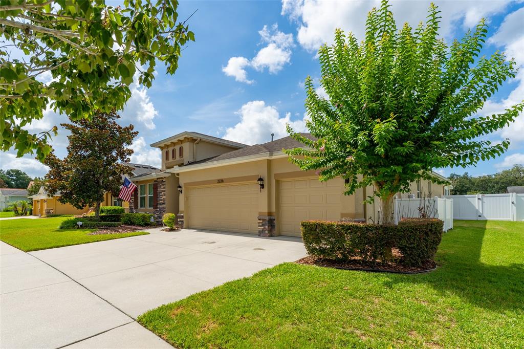 A tan house with a three-car garage, a manicured lawn, and a large tree — 2226 VALTERRA VISTA WAY, VALRICO, FL