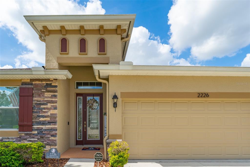 The exterior of a house features a tan stucco facade, a stone-accented wall, and a garage — 2226 VALTERRA VISTA WAY, VALRICO, FL