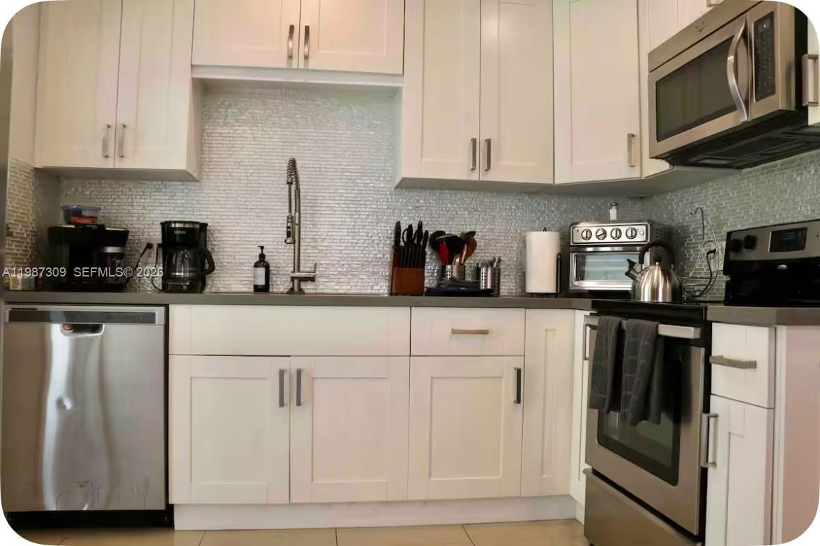 A kitchen features white shaker cabinets, stainless steel appliances, and a light-colored mosaic tile backsplash — 601 NW 116th St, Miami FL 33168, MIAMI, FL