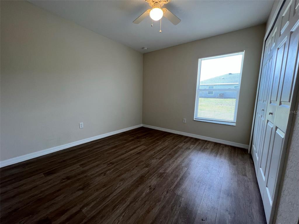 An empty bedroom features wood-look flooring, beige walls, a ceiling fan, and a white closet — 8526 JUNIPER ROAD UNIT 2, OCALA, FL