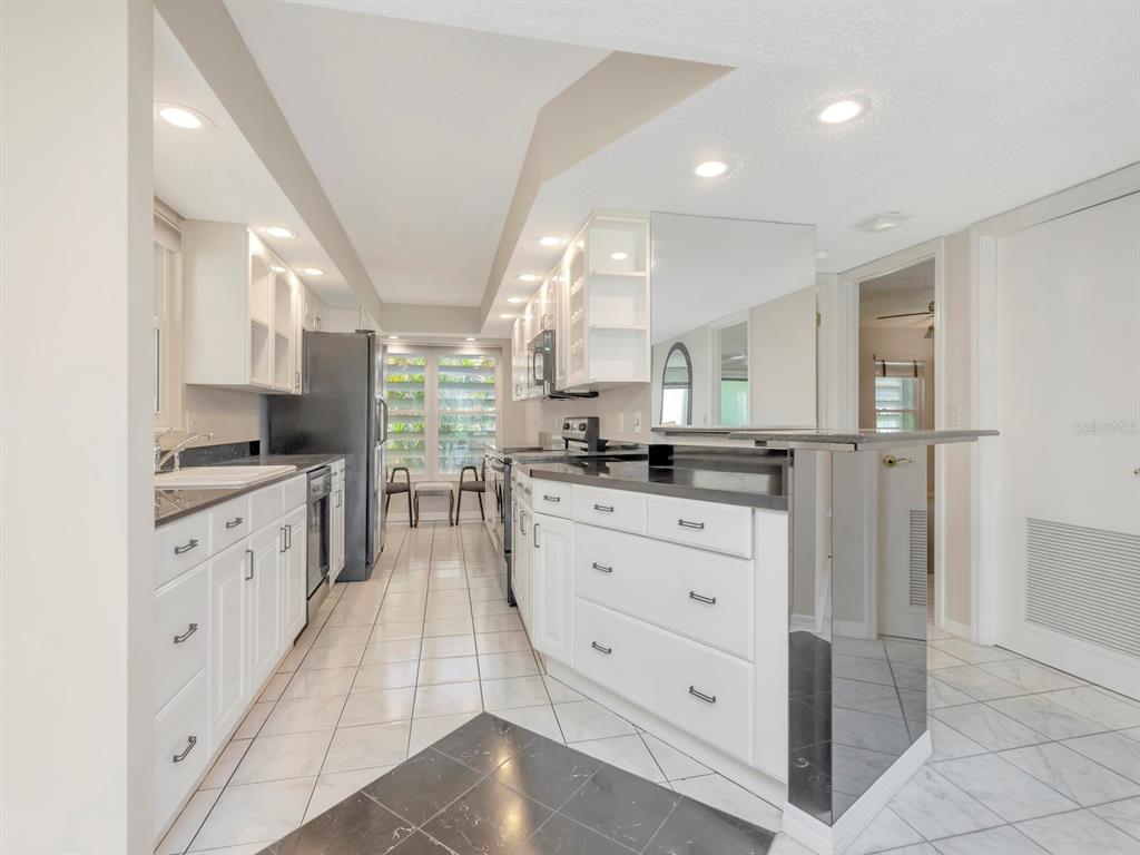 A galley-style kitchen features white cabinets, black countertops, a mirrored peninsula, and tiled flooring — 7871 SAILBOAT KEY BOULEVARD S UNIT 108, ST PETERSBURG, FL