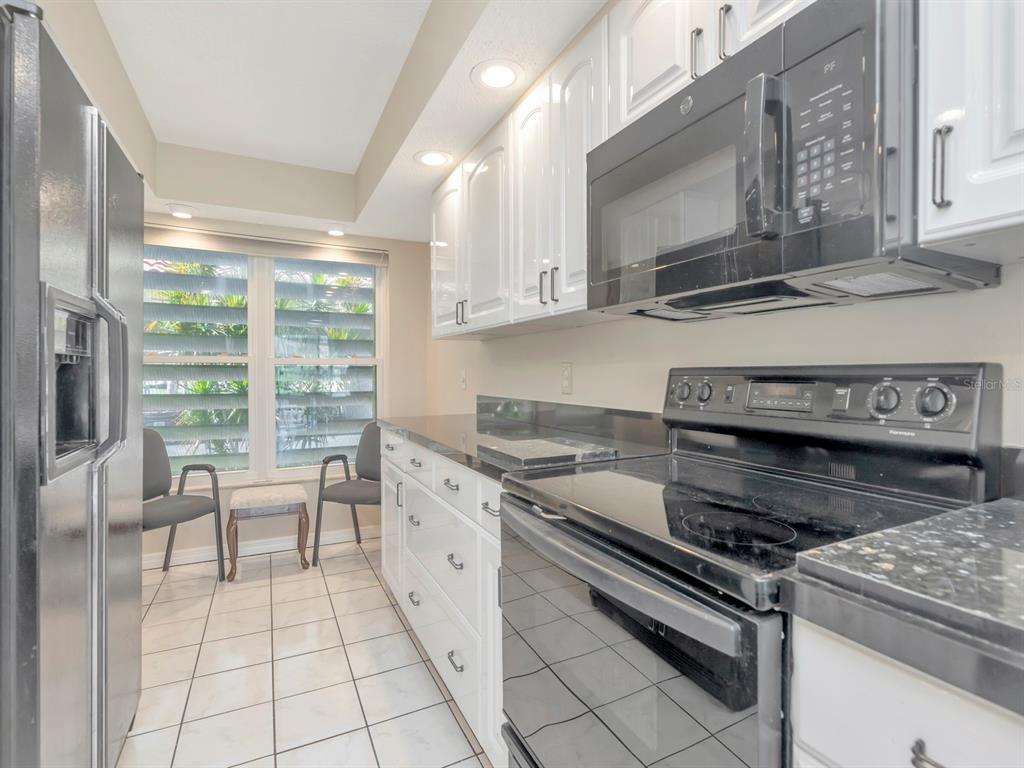 A galley kitchen features white cabinets, black appliances, dark countertops, and a windowed dining area — 7871 SAILBOAT KEY BOULEVARD S UNIT 108, ST PETERSBURG, FL