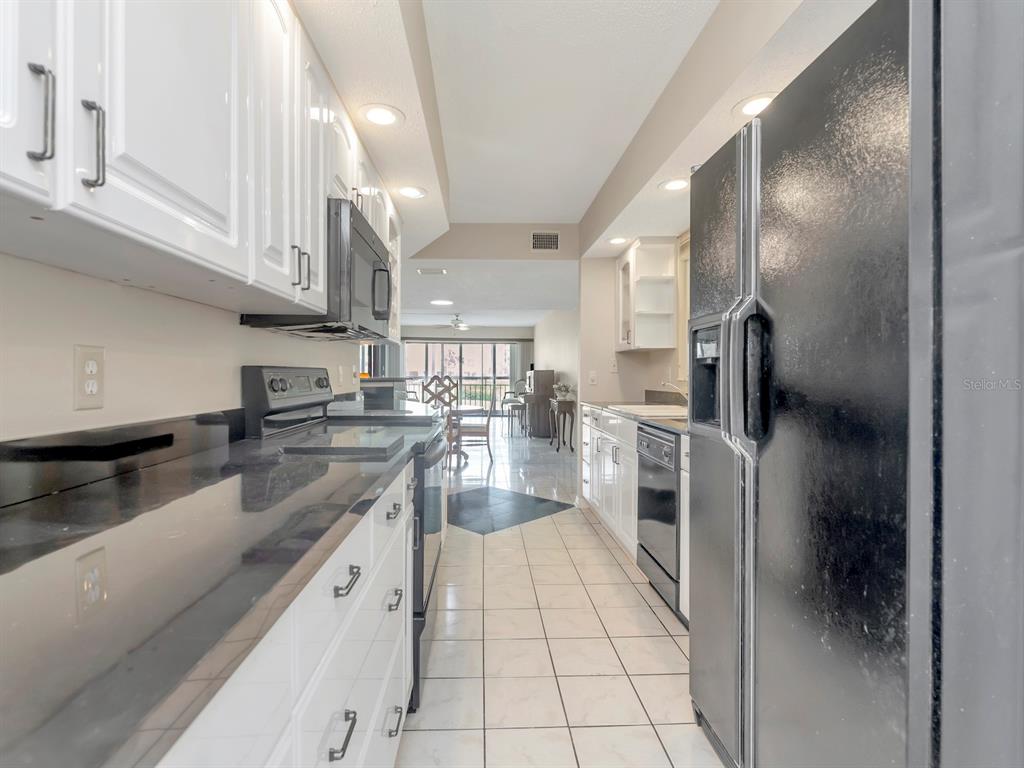 A galley kitchen features white cabinets, black countertops, and a black refrigerator — 7871 SAILBOAT KEY BOULEVARD S UNIT 108, ST PETERSBURG, FL