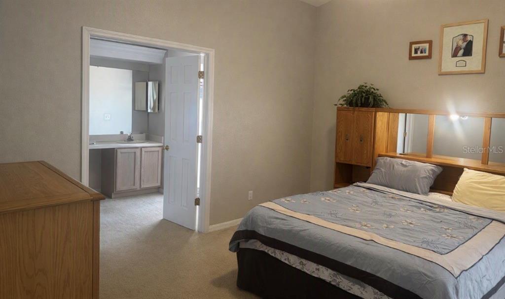 A bedroom with a bed, wooden headboard, and an open doorway leading to a bathroom — 27606 SKY LAKE CIRCLE, WESLEY CHAPEL, FL