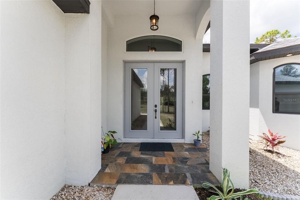 A covered entryway features a double glass door, stone tile flooring, and white stucco walls — 32706 OIL WELL ROAD, PUNTA GORDA, FL