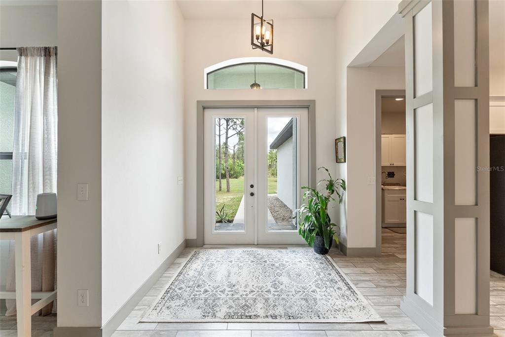 An entryway features a patterned rug, double glass doors, and a high ceiling with lighting — 32706 OIL WELL ROAD, PUNTA GORDA, FL