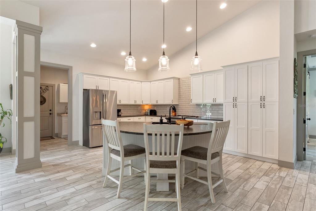 A kitchen features white cabinets, a curved island with three chairs, and wood-look tile flooring — 32706 OIL WELL ROAD, PUNTA GORDA, FL