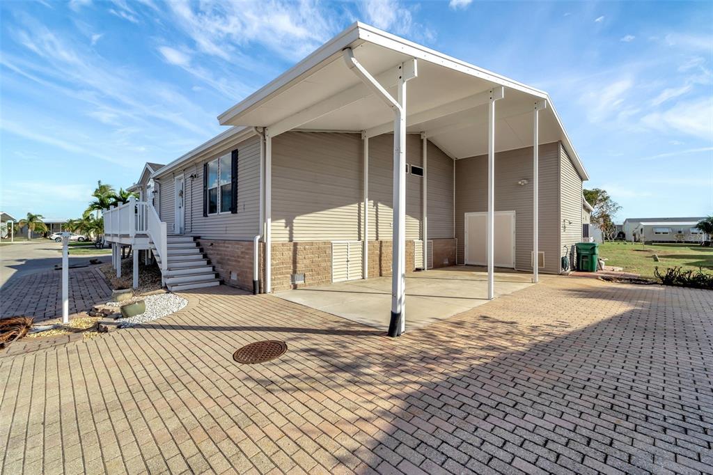 A mobile home with a covered carport, brick-paver driveway, and an elevated wooden deck entrance — 16 COPENHAGEN AVENUE, PUNTA GORDA, FL