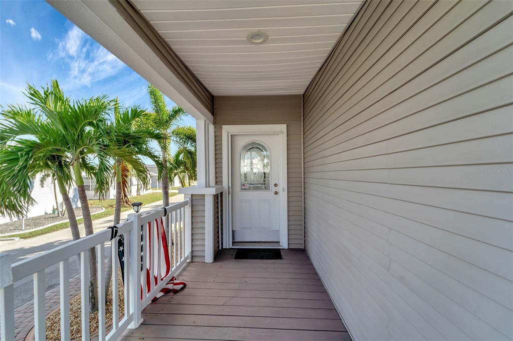A covered porch with light wood-look flooring, white railings, and a white front door — 16 COPENHAGEN AVENUE, PUNTA GORDA, FL