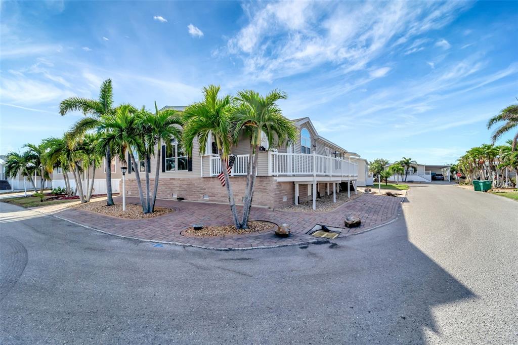 A tan manufactured home with a white porch and palm trees sits on a corner lot — 16 COPENHAGEN AVENUE, PUNTA GORDA, FL