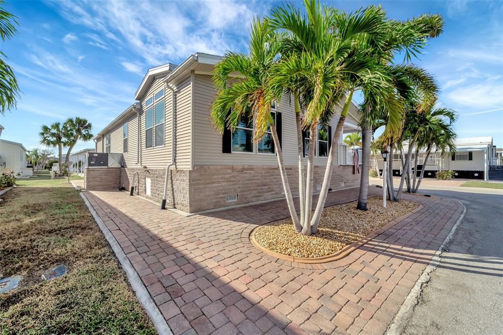 A light-colored manufactured home features a paver patio, palm trees, and stone-textured skirting — 16 COPENHAGEN AVENUE, PUNTA GORDA, FL