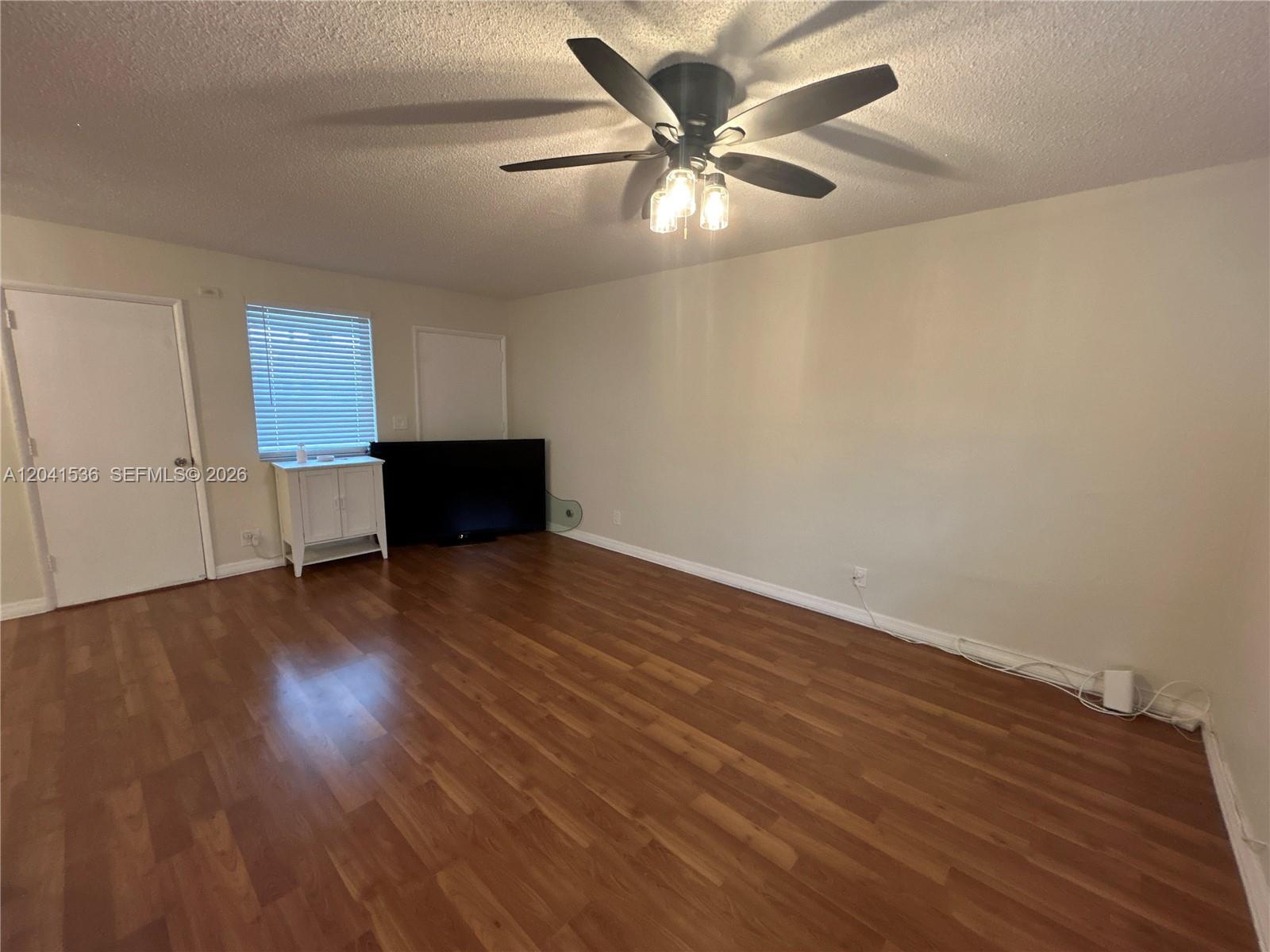 An empty room features wood-look flooring, a ceiling fan, and a television placed on the floor — 1717 Rodman St # 18, Hollywood FL 33020, HOLLYWOOD, FL