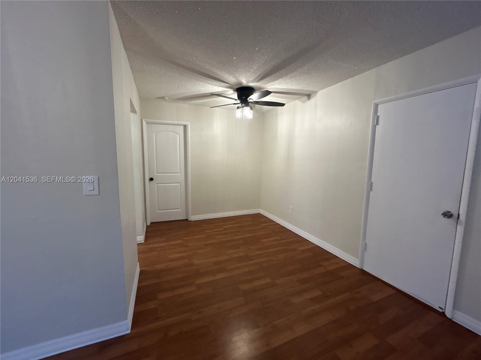 An empty room features wood-look flooring, white walls, a ceiling fan, and two white doors — 1717 Rodman St # 18, Hollywood FL 33020, HOLLYWOOD, FL