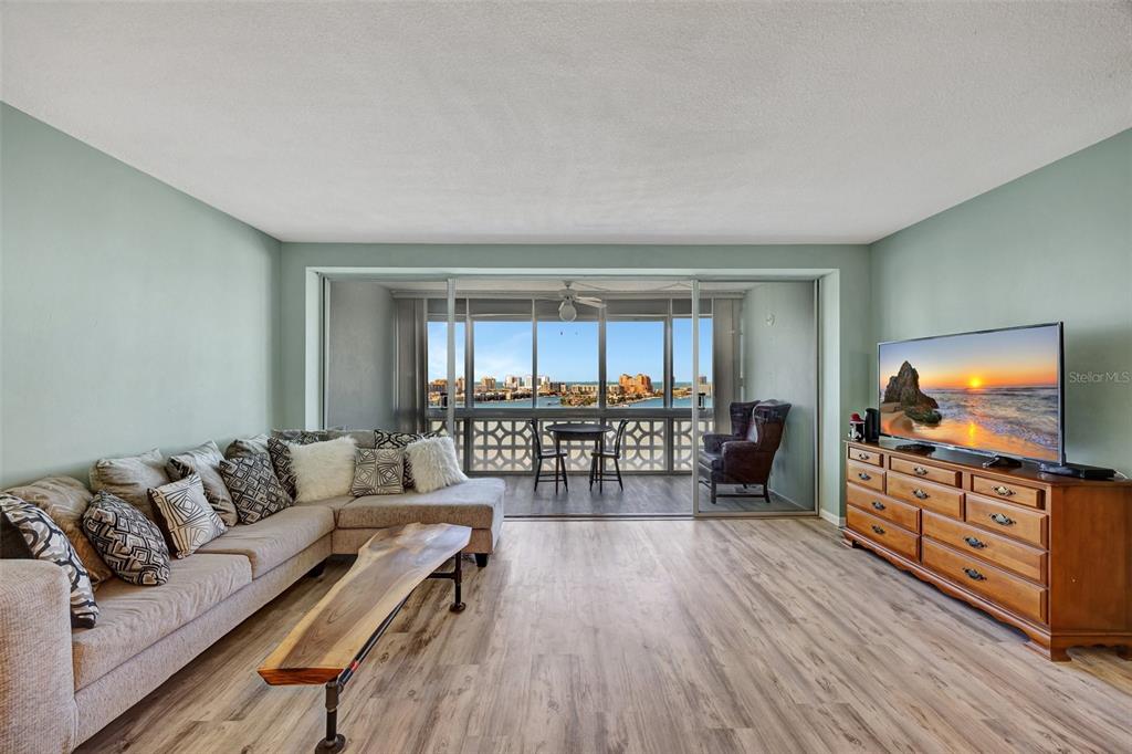 A living room with light wood flooring, a sectional sofa, and a balcony overlooking water — 31 ISLAND WAY UNIT 1403, CLEARWATER BEACH, FL