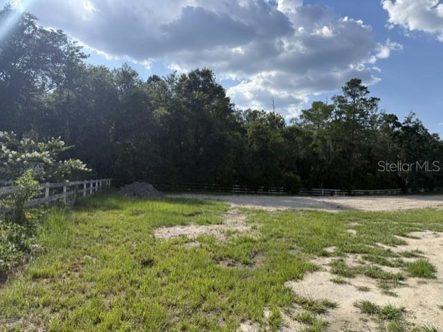 A grassy, partially cleared lot features a white fence bordering a dense line of trees — 420 NW 9TH AVENUE, LAKE BUTLER, FL