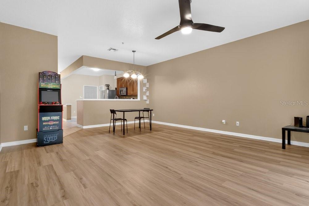 An open-concept dining area features light wood-look flooring, a ceiling fan, and an arcade cabinet — 6302 DAYSBROOK DRIVE UNIT 104, ORLANDO, FL