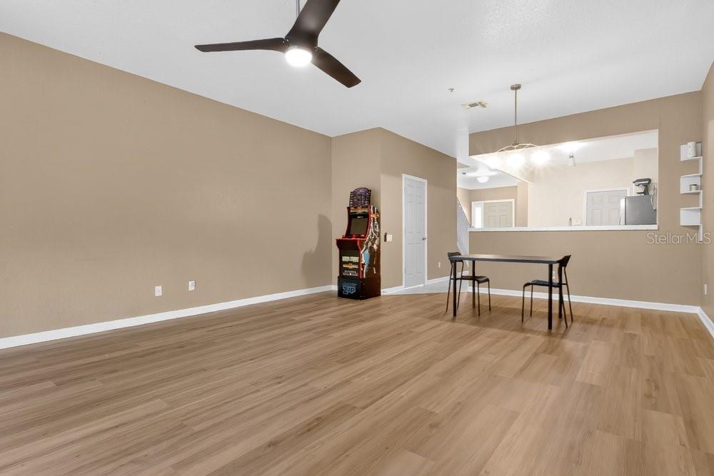 A room with light wood-look flooring, a ceiling fan, a dining table, and an arcade cabinet — 6302 DAYSBROOK DRIVE UNIT 104, ORLANDO, FL