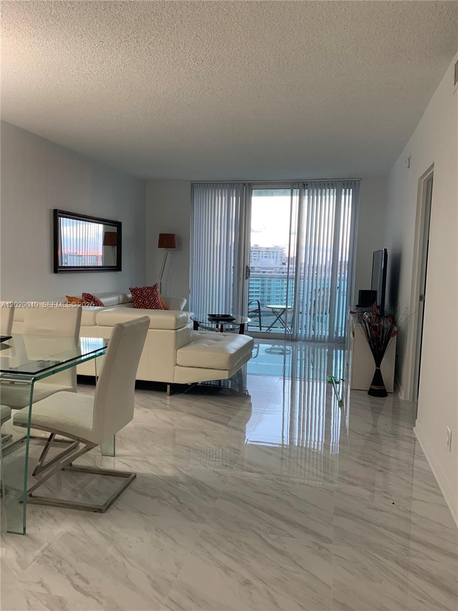 A living and dining area features white tile floors, a white sectional sofa, and balcony access — 3901 S Ocean Dr # 12V, Hollywood FL 33019, HOLLYWOOD, FL