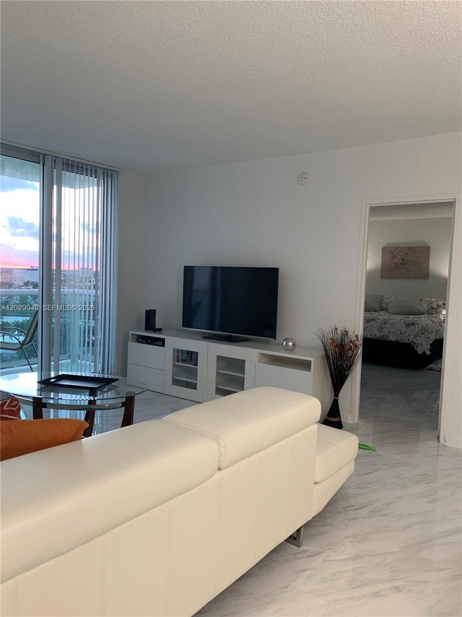 A living room features a white sofa, a television on a console, and marble flooring — 3901 S Ocean Dr # 12V, Hollywood FL 33019, HOLLYWOOD, FL