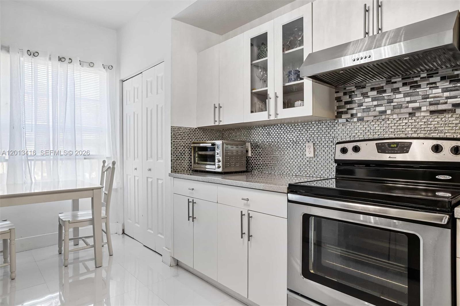 A kitchen features white cabinets, a mosaic tile backsplash, and a stainless steel stove — 746 NE 90th St # 606, Miami FL 33138, MIAMI, FL