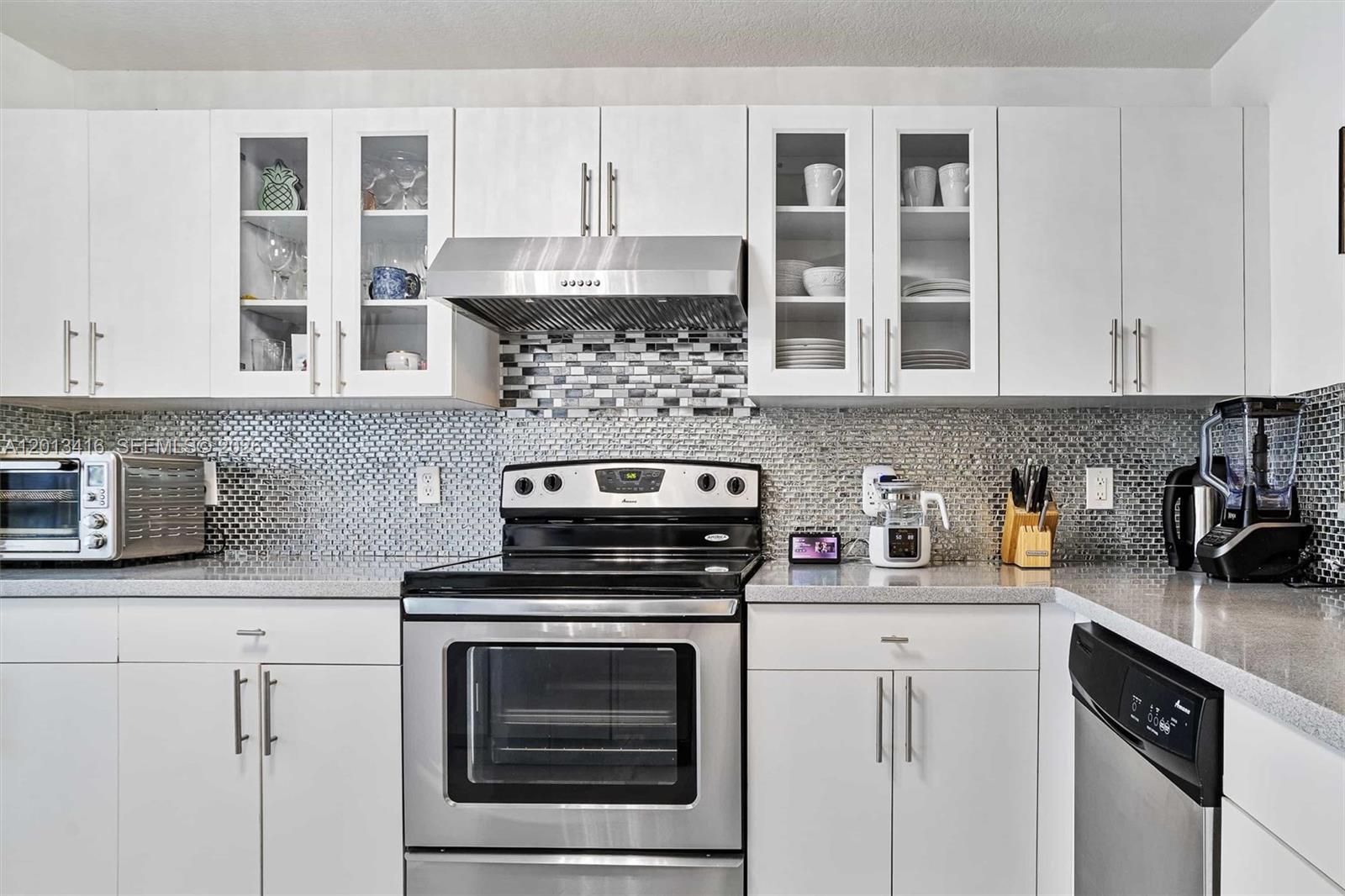A kitchen features white cabinets, stainless steel appliances, and a gray mosaic tile backsplash — 746 NE 90th St # 606, Miami FL 33138, MIAMI, FL