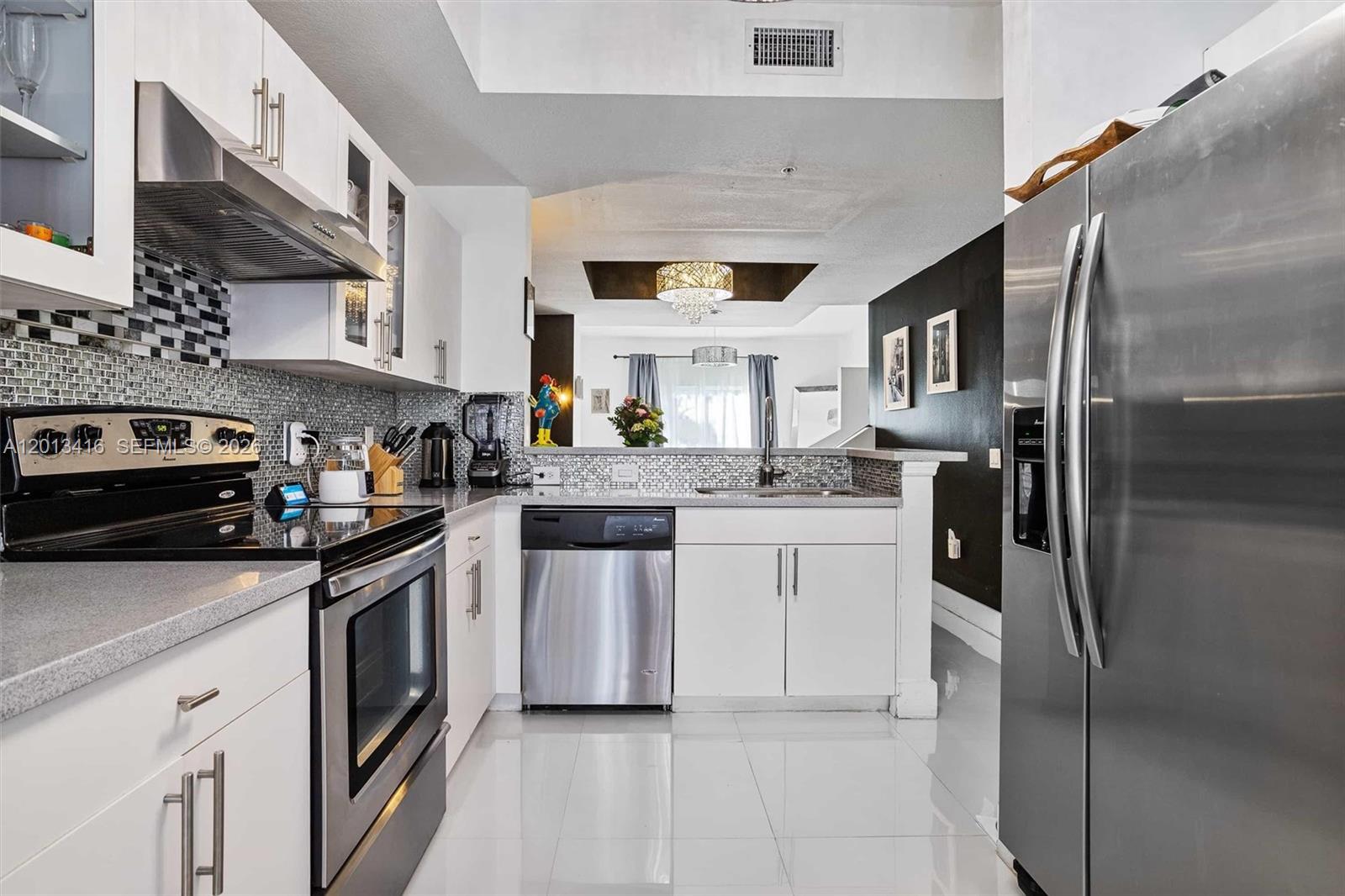 A modern kitchen features white cabinets, stainless steel appliances, and a gray tiled backsplash — 746 NE 90th St # 606, Miami FL 33138, MIAMI, FL