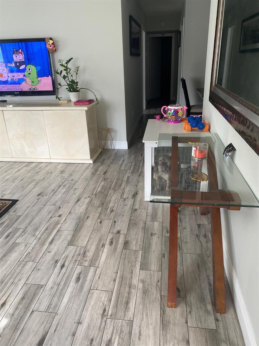 A living room features light wood-look tile flooring, a television console, and a glass-topped table — 225 SW 7th Street # 101, Boca Raton FL 33432, BOCA RATON, FL