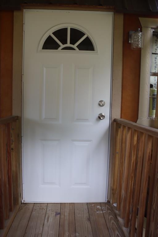 A white front door with a semi-circular window sits on a wooden porch — 117 FRONTENAC STREET, INTERLACHEN, FL
