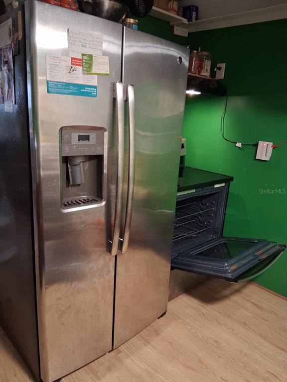 A stainless steel side-by-side refrigerator stands next to an open oven in a kitchen — 117 FRONTENAC STREET, INTERLACHEN, FL
