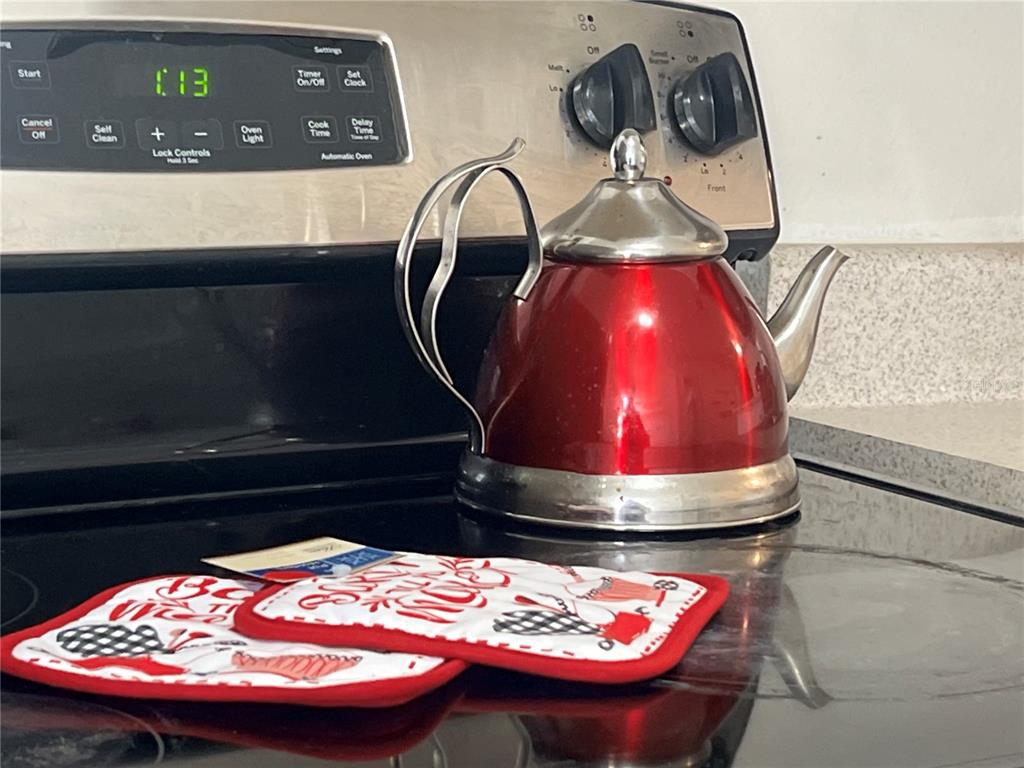 A red tea kettle and two oven mitts sit on a black glass stovetop — 1322 ARLINGTON STREET, ORLANDO, FL