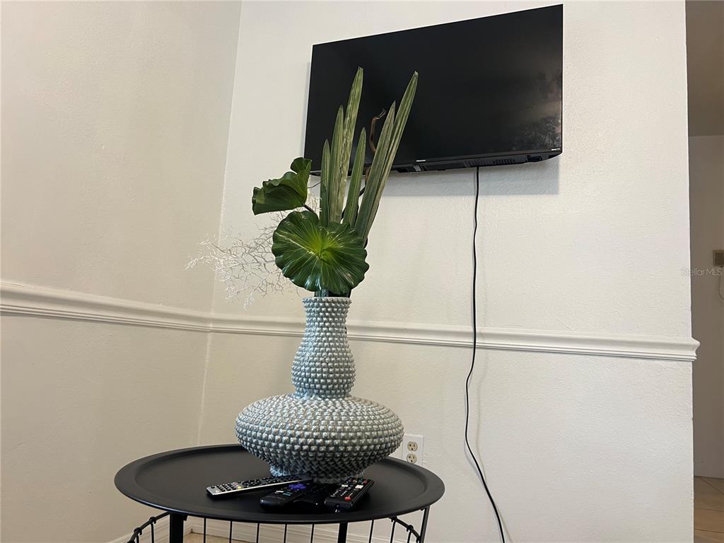 A textured gray vase with greenery sits on a black table below a wall-mounted television — 1322 ARLINGTON STREET, ORLANDO, FL