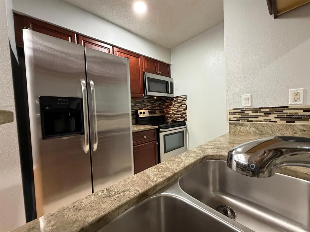 A kitchen features stainless steel appliances, dark wood cabinets, and a granite countertop with sink — 8643 MALLARD RESERVE DRIVE UNIT 202, TAMPA, FL